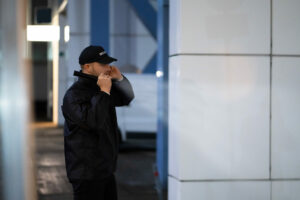 Security Guard Walking Building Perimeter With Flashlight At Night